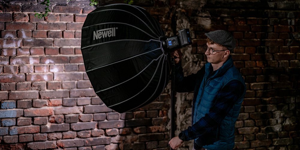 Softbox paraboliczny Newell 85 cm w trakcie przestawiania statywu z zamontowaną lampą i softboxem