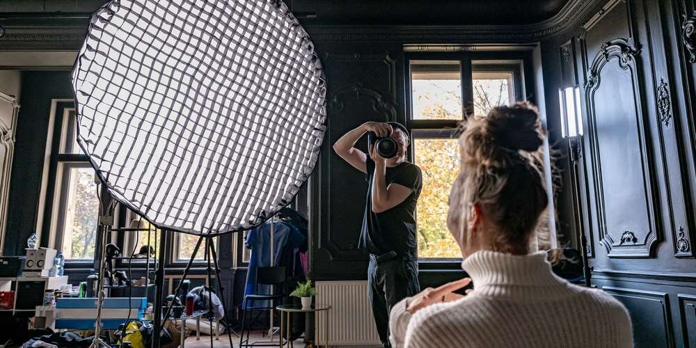 Fotograf wykonuje zdjęcie modelce oświetlonej parabolicznym softboxem Newell 120 cm z założoną siatką typu grid