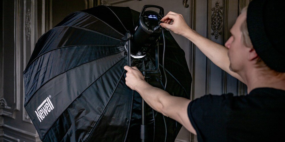 Fotograf ustawia lampę studyjną z zamontowanym parabolicznym softboxem Newell 120 cm w czarnym pokrowcu z logo marki