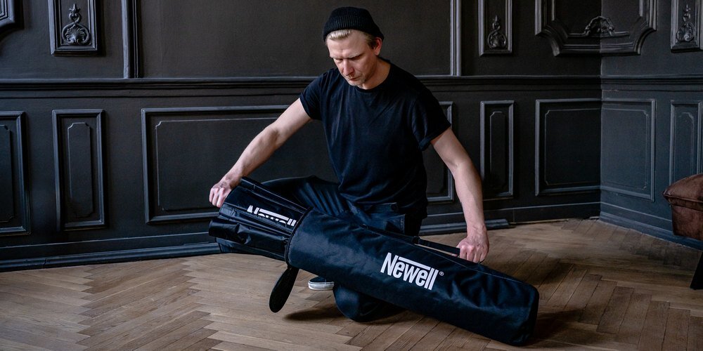 Fotograf pakuje paraboliczny softbox Newell 120 cm do czarnego pokrowca z logo marki, przygotowując sprzęt do transportu