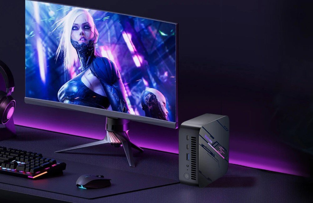 Komputer BLACKVIEW MP100 Komputer mini stojący pionowo obok monitora z wyświetloną postacią z gry, w otoczeniu klawiatury, myszy i podświetlenia w fioletowych barwach, porty, złącza
