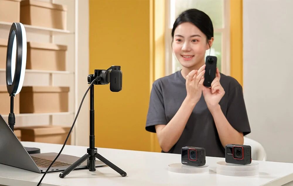 INSTA360 Link 2 Insta360 Link 2 technologię Phase Detection Auto Focus (PDAF), autofokusa PDAF  - Kobieta prezentująca małą kamerę podczas nagrania przy biurku z dodatkowym oświetleniem i sprzętem wideo