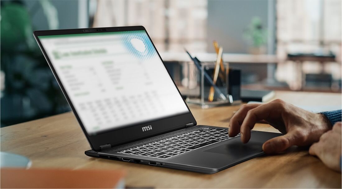 Laptop MSI Prestige 14 AI Studio na biurku, ekran z rozmytym widokiem arkusza kalkulacyjnego – ilustracja funkcji Tobii Aware chroniącej prywatność na ekranie. - Tobii Aware