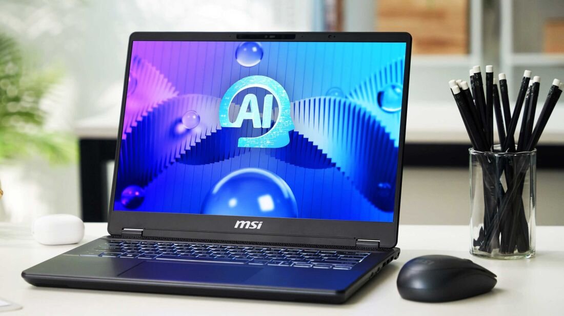 Laptop MSI Prestige 14 AI Studio na jasnym biurku, ekran z grafiką AI, mysz MSI obok, szklany pojemnik z ołówkami, jasne tło biurowe. - Opis serii Prestige