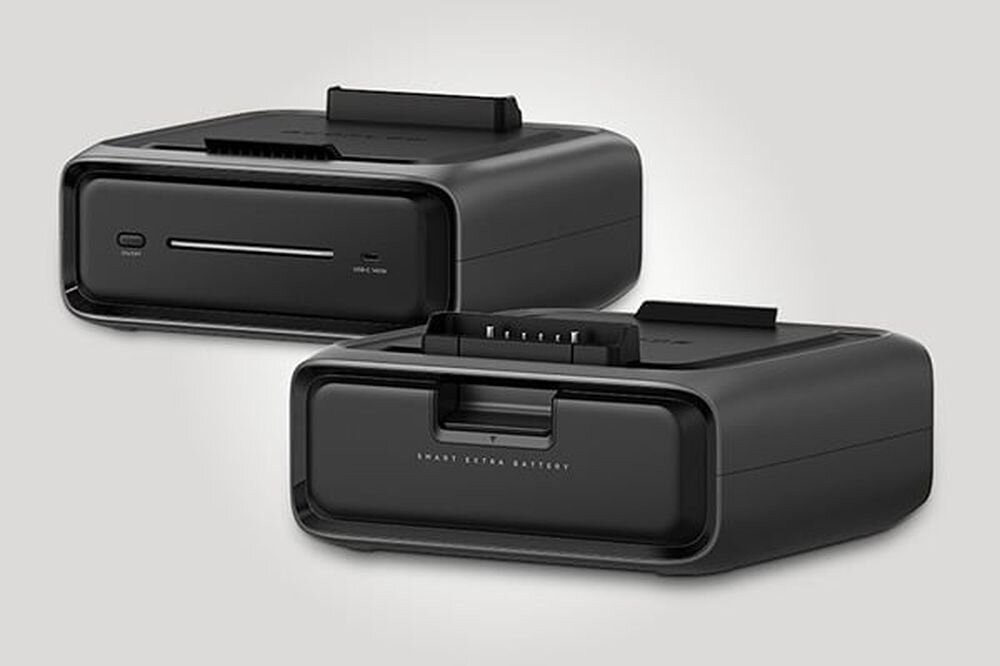 Na obrazie widoczne są dwie czarne baterie o prostokątnym kształcie z napisem \'SMART EXTRA BATTERY\'. Jedna z baterii ma widoczne złącze na górze, a druga posiada przyciski i porty na przedniej stronie.