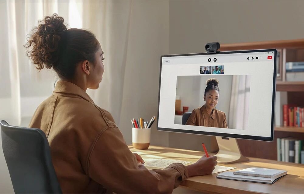insta360 Link 2C insta360 Link 2C dołączone do zestawu Recognition Markers oprogramowanie Link Controller AI - Kobieta siedząca przy biurku z długopisem w dłoni i prowadząca rozmowę wideo na szerokim monitorze