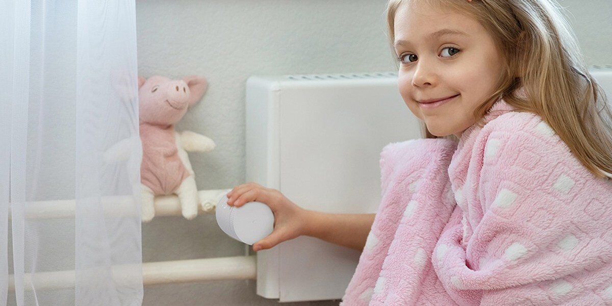 Głowica termostatyczna IMOU IOT-TRV1, ciepło, regulacja, ogrzewanie, oszczędność, dziewczynka trzyma głowicę zamontowaną do kaloryfera