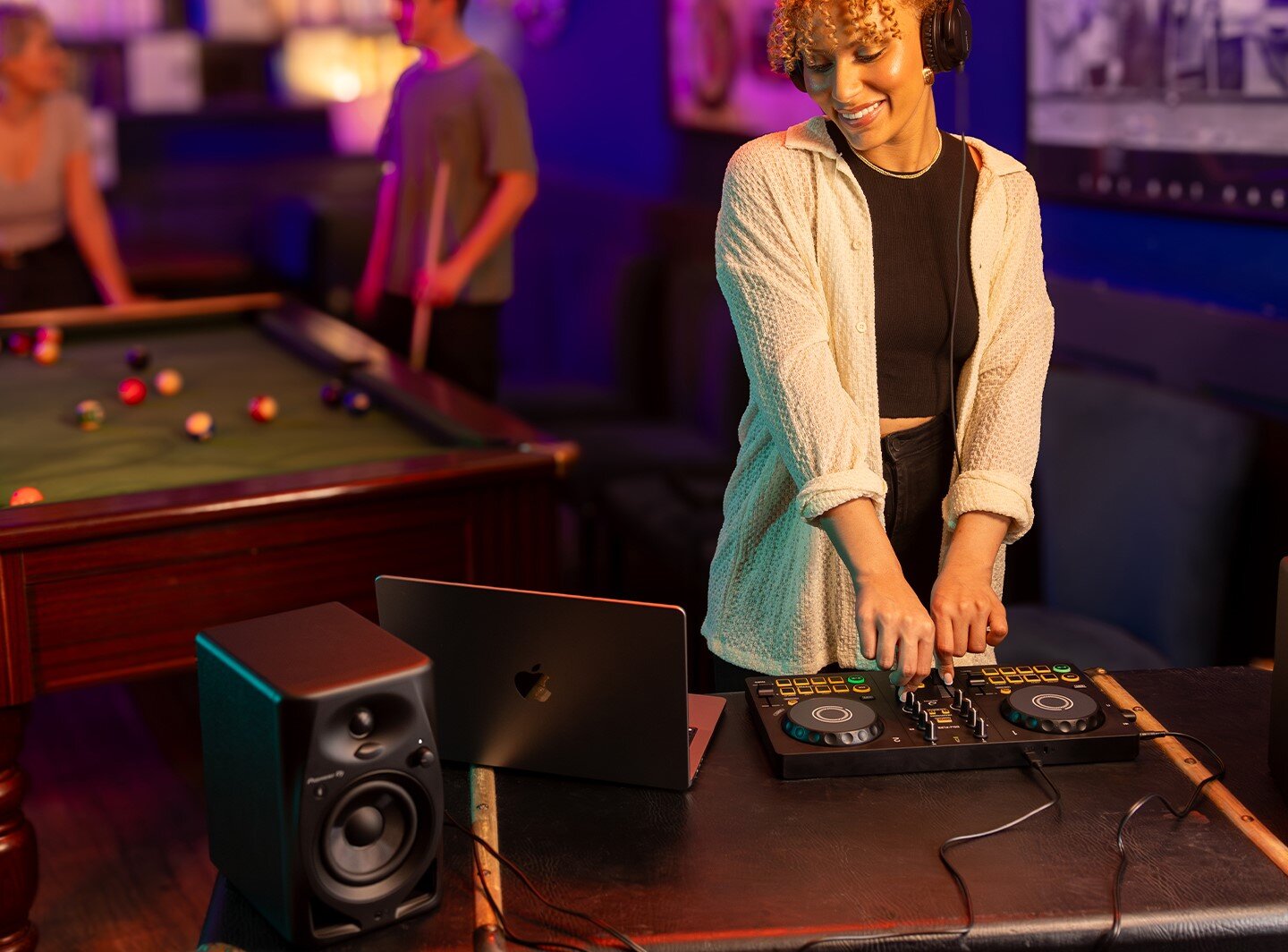 Kontroler DJ ALPHA THETA DDJ-FLX2 - Kompatybilność z aplikacjami, kobieta stoi przy kontrolerze, patrząc na laptopa, które stoją na stole. w tel ludzie grający w bilard