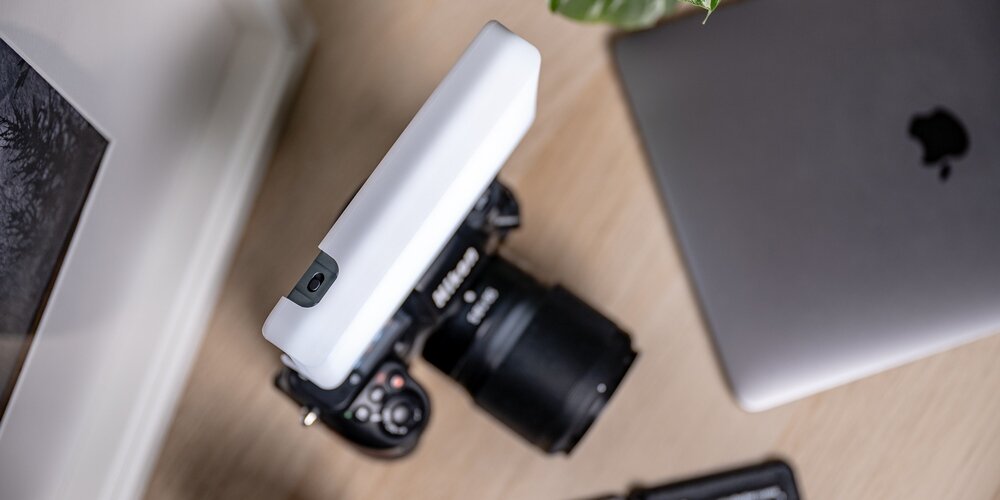 Lampa Newell LED RGB-W Rangha zamocowana na aparacie fotograficznym, leżącym na biurku obok laptopa i rośliny