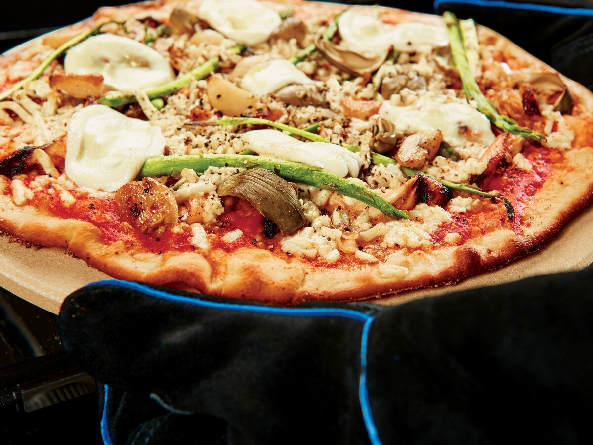 Kamień do pizzy BROIL KING 33 cm, kamień, pizza, spód, chrupiący, Pizza na patelni z cebulą, pomidorami i serem na drewnianej desce obok grilla.