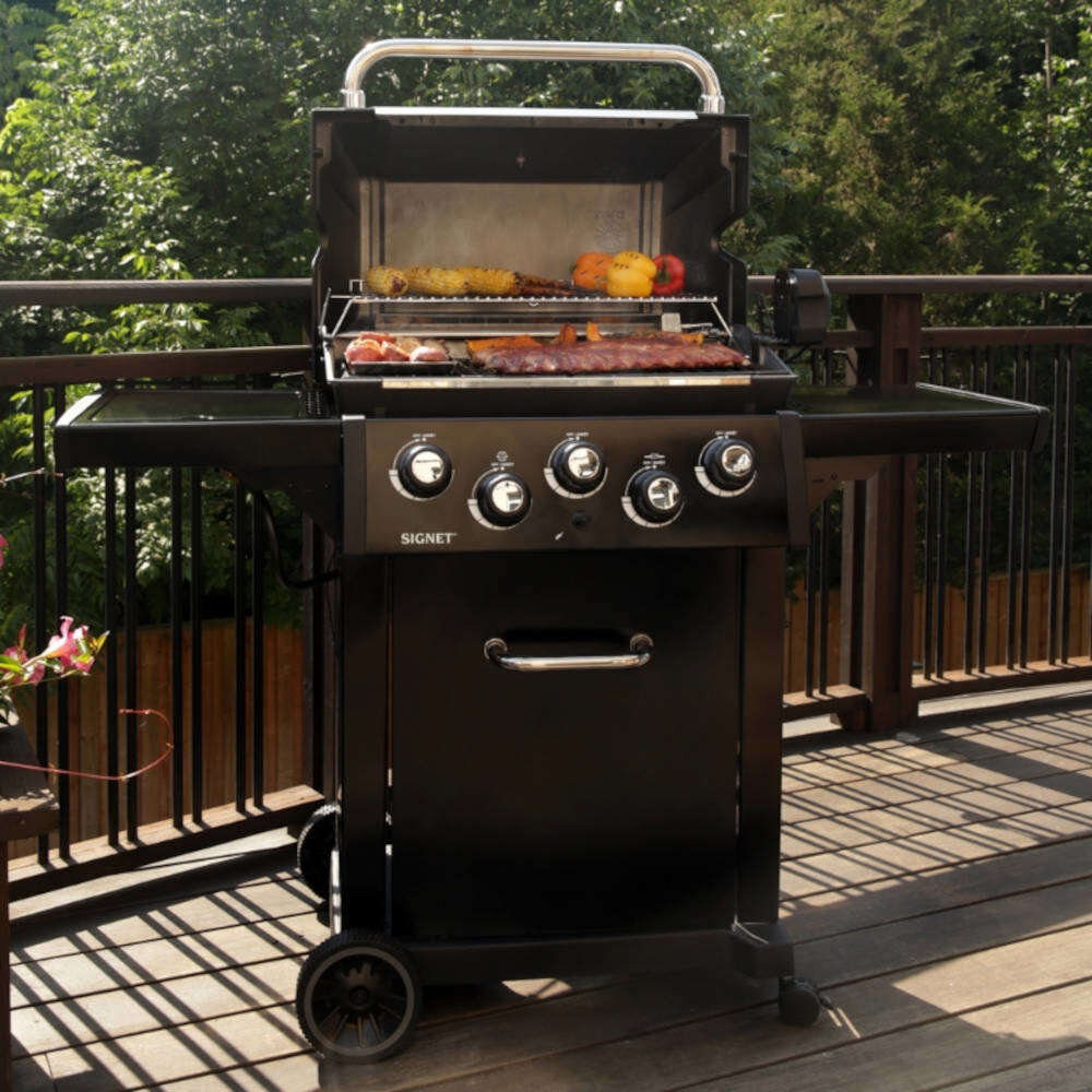 Grill gazowy BROIL KING Signet 390 Shadow 11.4 kW 65 x 38 - 60 x 26 cm grill na drewnianym tarasie w tle drzewa grillowanie soczyste potrawy smak relaks spotkania
