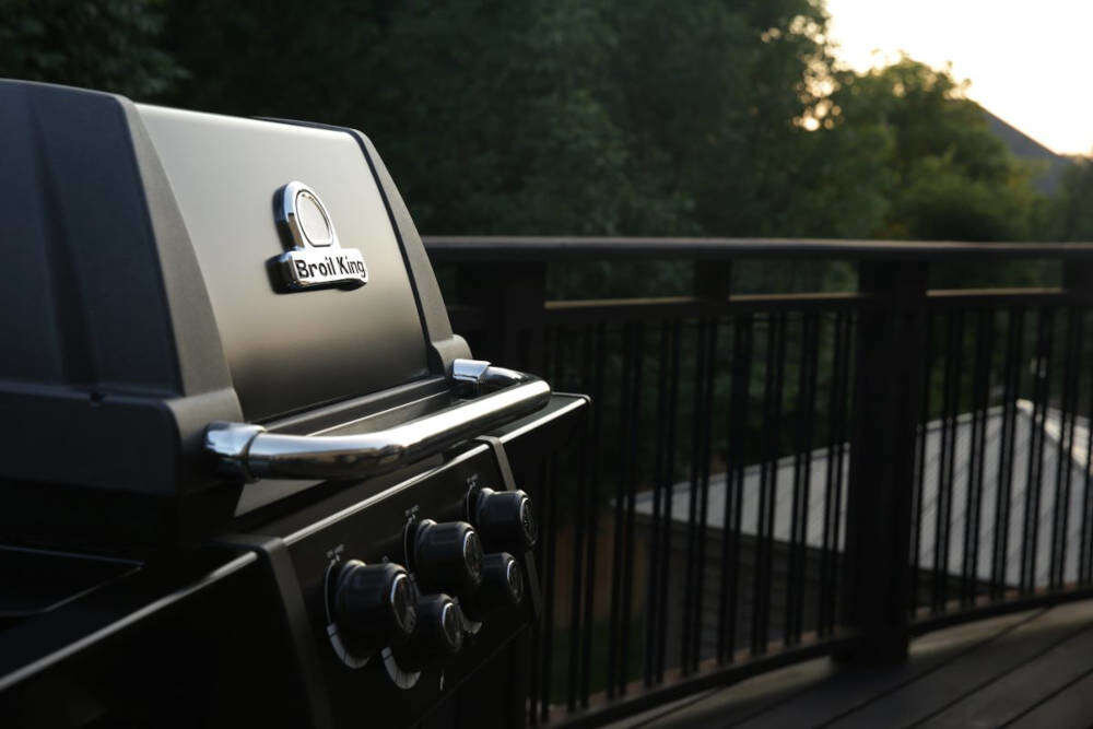 Grill gazowy BROIL KING Signet 390 Shadow 11.4 kW 65 x 38 - 60 x 26 cm zbliżenie na pokrywę grilla grill na tarasie w tle drzewa elegancki design funkcjonalność solidna konstrukcja ze stali szlachetnej czarna farba proszkowa sprawdzone rozwiązania technologiczne intuicyjna i prosta obsługa dla osób rozpoczynających przygodę z grillowaniem i doświadczonych miłośników BBQ