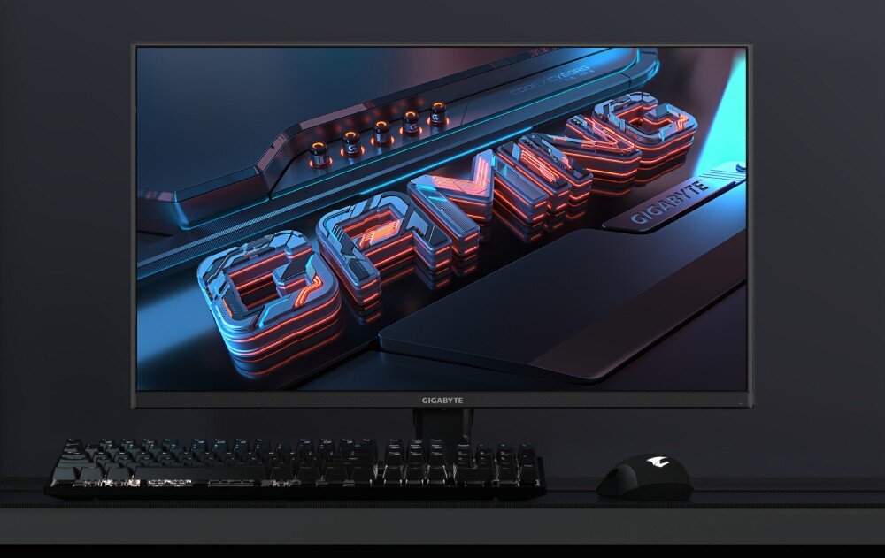 Monitor GIGABYTE GS27U Monitor z włączonym ekranem prezentującym trójwymiarowy napis 'GAMING' w stylu neonowym, stojący na biurku obok klawiatury i myszy, opis
