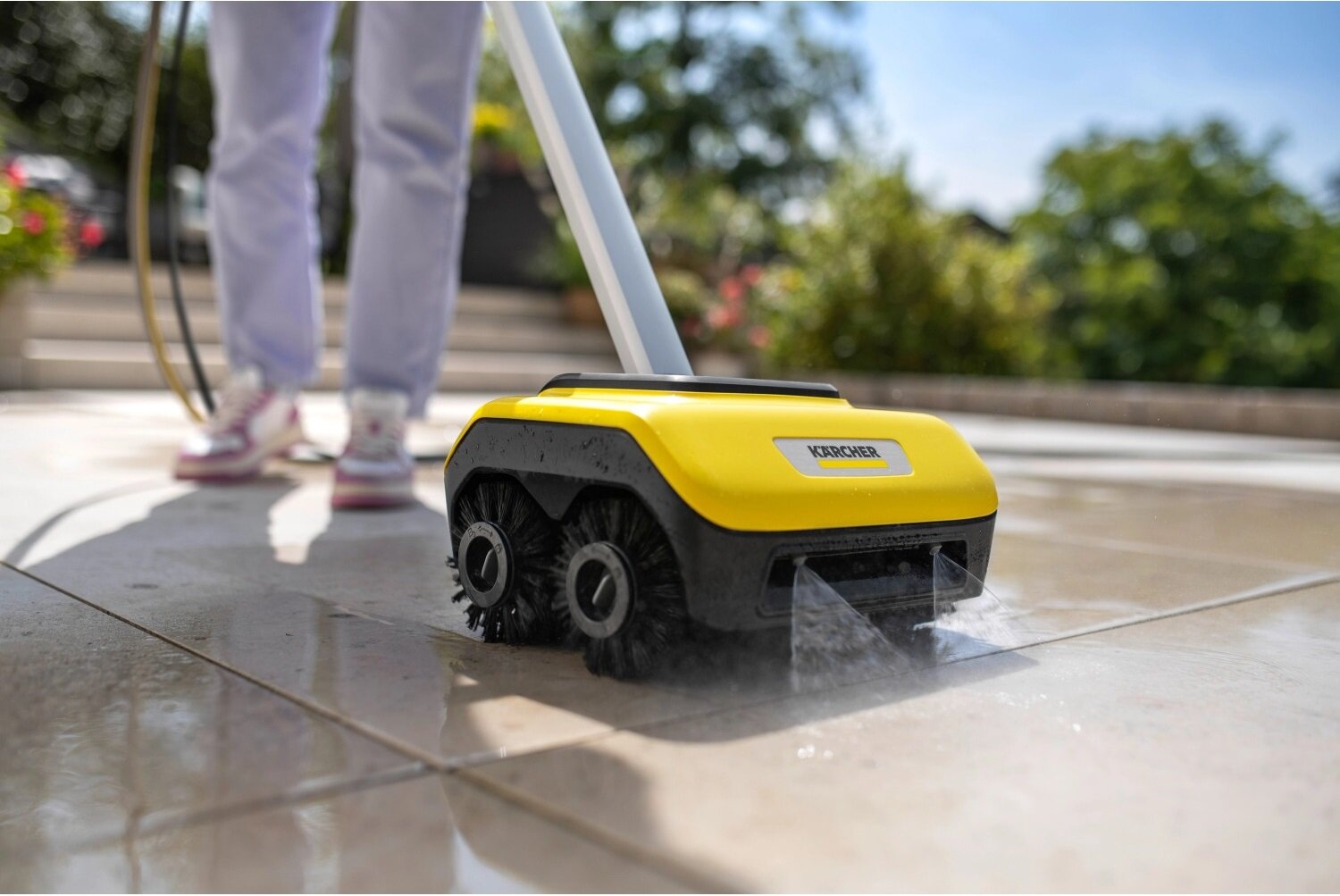 Urządzenie do czyszczenia posadzek KARCHER z żółtą obudową i czarnymi szczotkami, używane na zewnętrznej powierzchni. Widoczne logo \'KARCHER\' na obudowie.