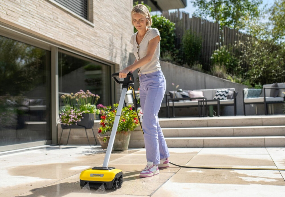 Osoba używa urządzenia do czyszczenia posadzek na tarasie. Urządzenie ma żółty kolor i widoczne jest logo KARCHER.