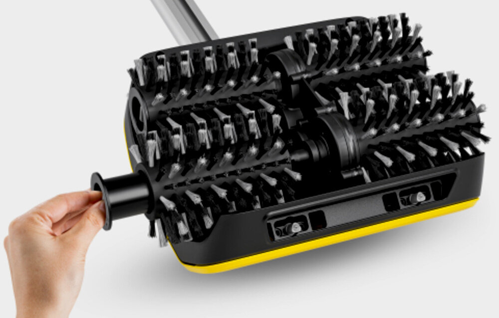 Urządzenie do czyszczenia posadzek z dwoma obrotowymi szczotkami i żółtym akcentem. Ręka trzyma element urządzenia, które ma czarną obudowę.
