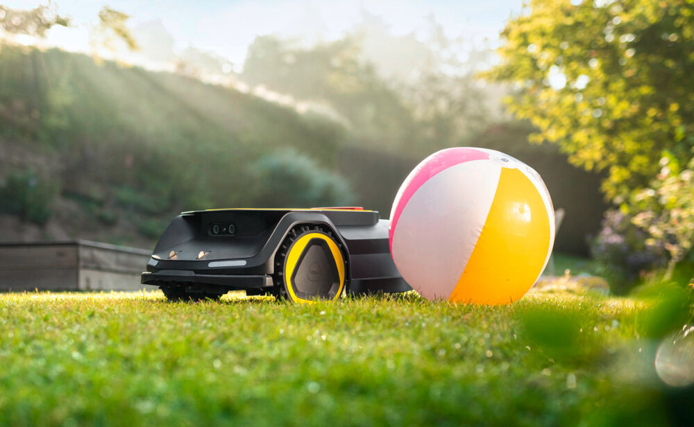Robot koszący KARCHER RCX 6 1.269-760.0 sterowanie Wi-Fi-Bluetooth robot na trawie obok piłka w tle ogród kamera 3D system AI rozpoznają powierzchnie ludzi i zwierzęta dopasowuje trasę do otoczenia unika zderzeń z obiektami dostosowuje pracę do warunków bezpieczną i inteligentną nawigację w zróżnicowanym terenie wspomaga pracę w sytuacjach gdy sygnał GPS jest słaby