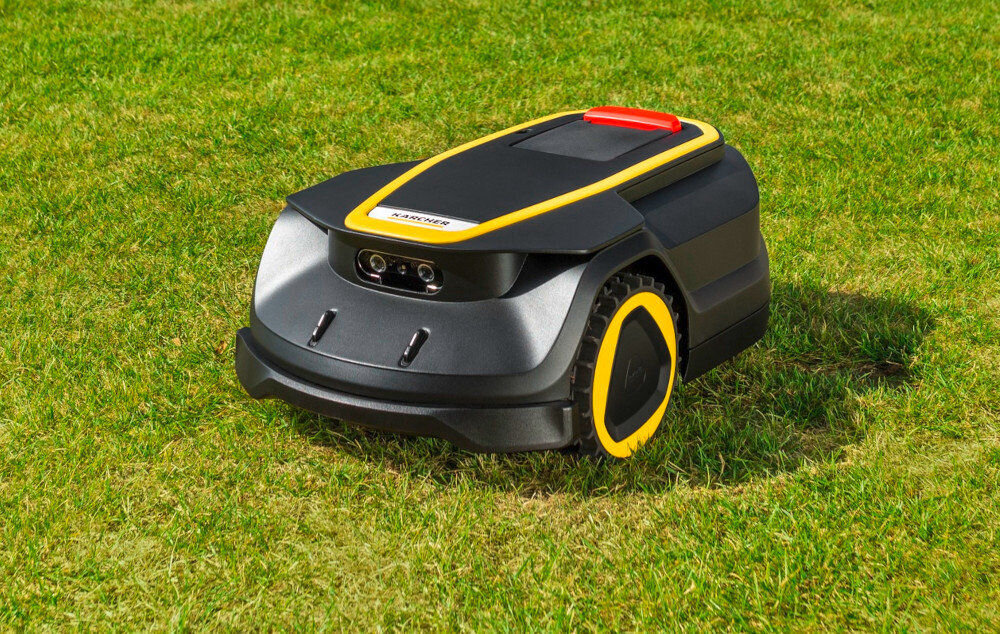 Robot koszący na trawie, w kolorze czarnym z żółtymi akcentami i czerwonym elementem na górze. Widoczne logo \'KARCHER\' na przedniej części urządzenia.