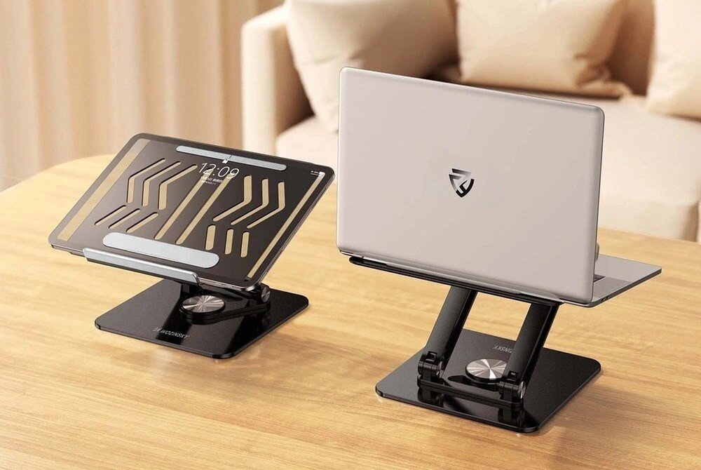 Na drewnianym stole znajdują się dwie czarne podstawki pod laptopa marki WOZINSKY, jedna z tabletem, druga z laptopem. Na ekranie tabletu widoczna jest godzina 12:09.