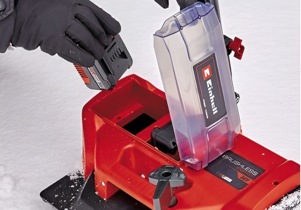 Odśnieżarka EINHELL GE-ST 36-40 Li E-Solo śnieg podłoże osoba wkłada akumulator do wnętrza odśnieżarki widok na pokrywę zabezpieczającą akumulator pokrywa baterii zamykana na magnes chroni akumulatory przed śniegiem oraz wilgocią bezpieczeństwo zasilania i stabilność działania dłuższa żywotność spokojniejsze użytkowanie