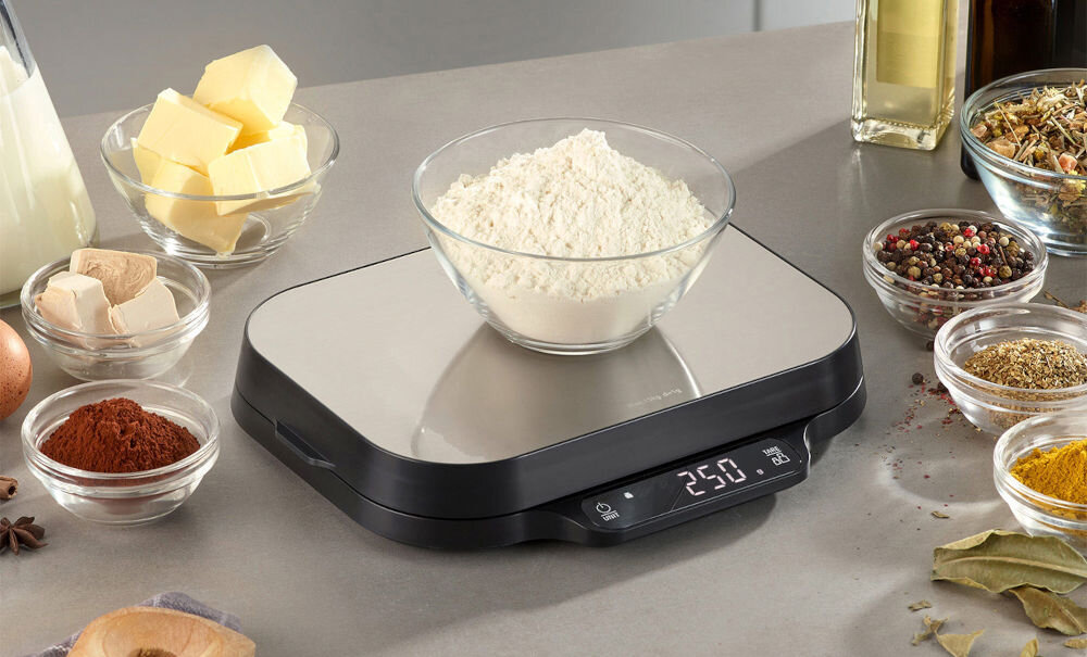 Waga kuchenna CASO KitchenDuo precyzyjne ważenie waga wyświetlacz przyciski czarno srebrna na wadze stoi miska z mąką obok wagi produkty z miseczkach