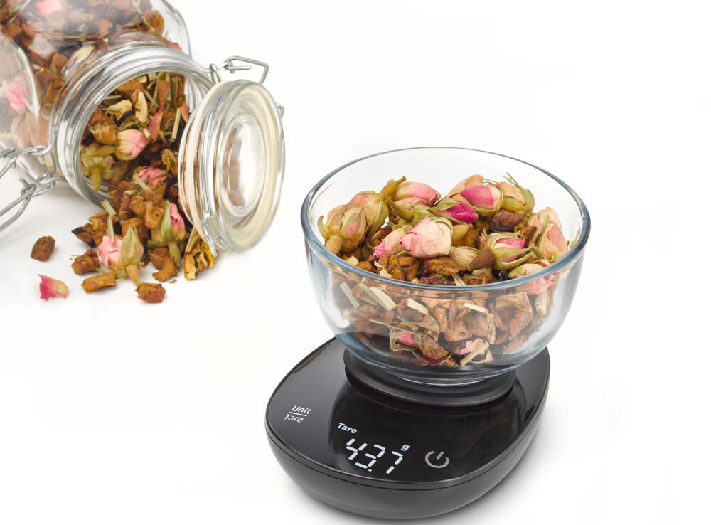 Waga CASO FinoCompact czarna waga na wadze stoi miseczka z kwiatami obok lezy słoik z kwiatami wyświetlacz przyciski białe tło  do odmierzania niewielkich ilości składników przyprawy, kawa, herbata leki zakres pomiaru od 0,1 g do 500 g dokładność funkcja tary praktyczne narzędzie w kuchni Obsługa różnych jednostek miary gramy mililitry uncje elegancki design funkcjonalność 