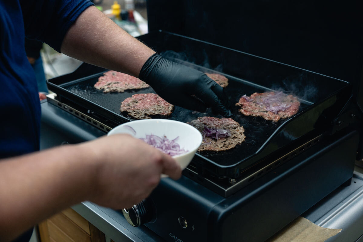 Grill gazowy CAMPINGAZ Plancha Sigma 2 cook, sposoby, pieczenie, pośrednie, duszenie, osoba przygotowuje posiłki na grillu