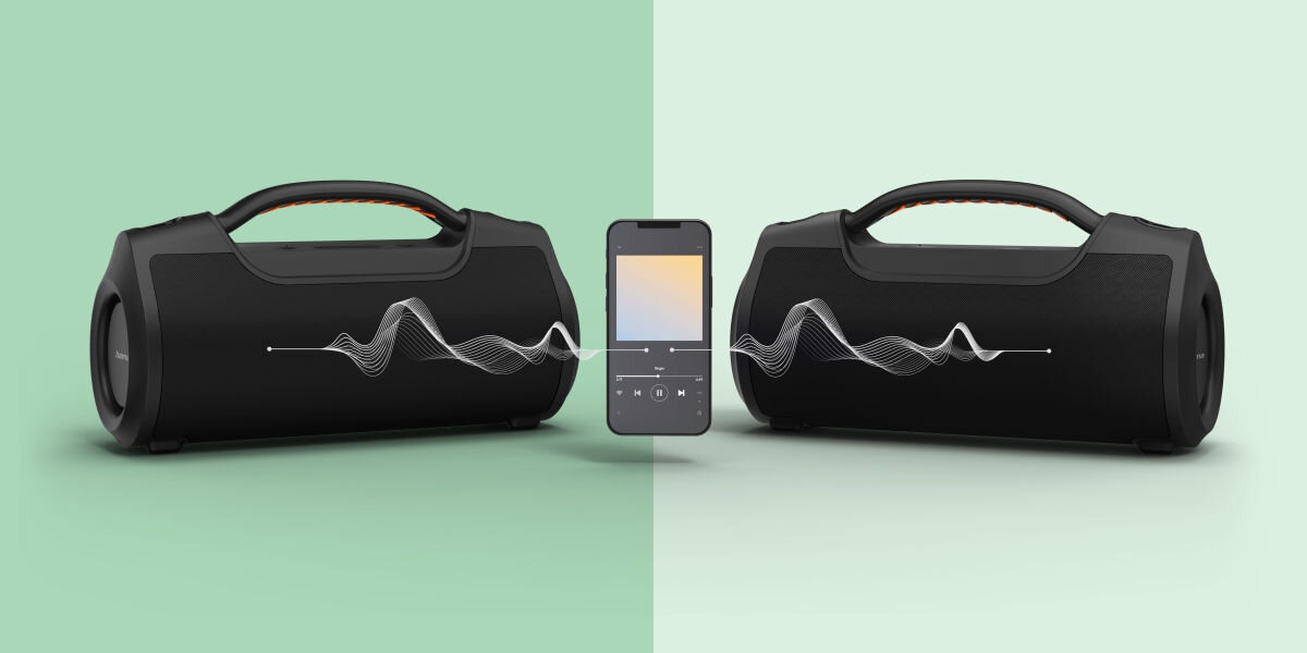 Na obrazie znajdują się dwa czarne głośniki mobilne oraz smartfon pomiędzy nimi. Głośniki mają uchwyty na górze, a z ekranu smartfona wychodzą fale dźwiękowe w kierunku głośników.