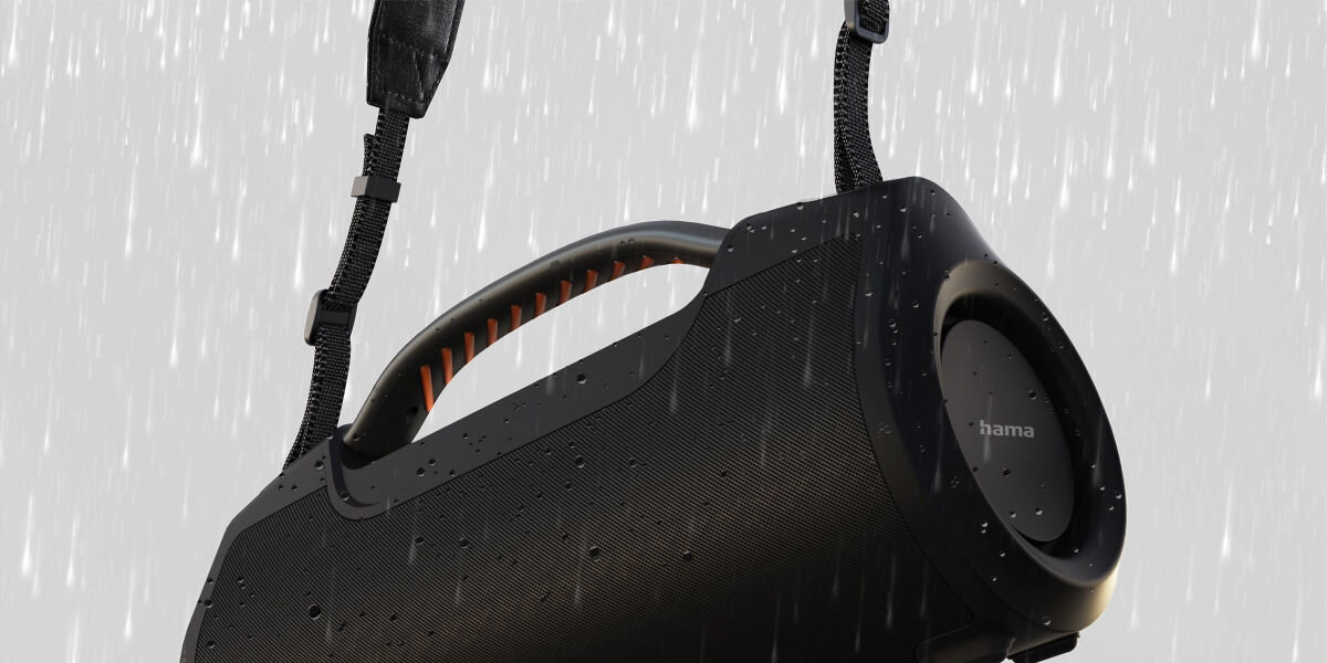 Czarny głośnik mobilny z logo \'hama\' na boku, zawieszony na pasku w deszczu. Obudowa głośnika pokryta jest kroplami wody.