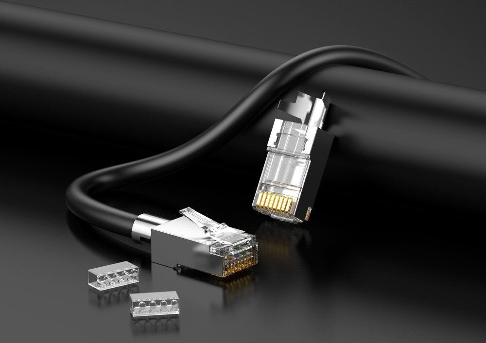 Wtyk UGREEN 70316 Zdjęcie przedstawia dwa ekranowane wtyki RJ45 oraz dwa małe, przezroczyste elementy pozycjonujące przewody na czarnym, gładkim tle. Jeden z wtyków jest zarobiony na czarnym kablu i leży poziomo, a drugi stoi pionowo obok grubszego, czarnego wałka