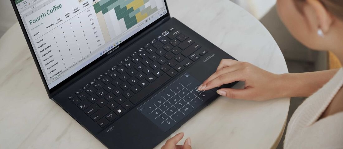Kobieta obsługująca laptop ASUS ZenBook UM3402 przy okrągłym stole, ekran z arkuszem kalkulacyjnym, dotykowy panel numeryczny w touchpadzie – klawiatura ASUS ErgoSense.