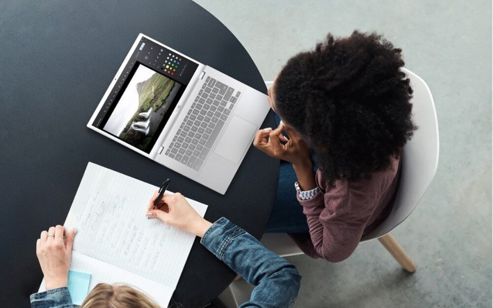 Laptop ASUS Chromebook Plus CX3402CVA Widok z góry na otwarty laptop i dwoje ludzi siedzących przy okrągłym stole. Jedna osoba pisze w zeszycie, druga przygląda się ekranowi, bateria, łączność Wi-Fi