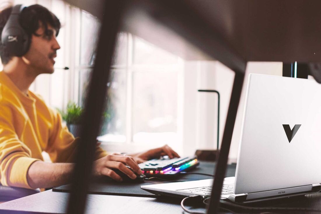 Laptop HP Victus 15 - Mężczyzna w słuchawkach siedzi przy biurku z laptopem, zaangażowany w aktywność związana z technologią. System audio B&O i HP Audio Boost 
