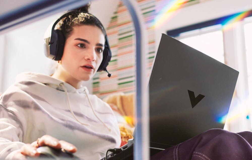 Laptop HP Victus 15 - Kobieta w białej bluzie i słuchawkach siedzi w autobusie z laptopem, skupiona na pracy lub relaksie. Ekologia w technologii