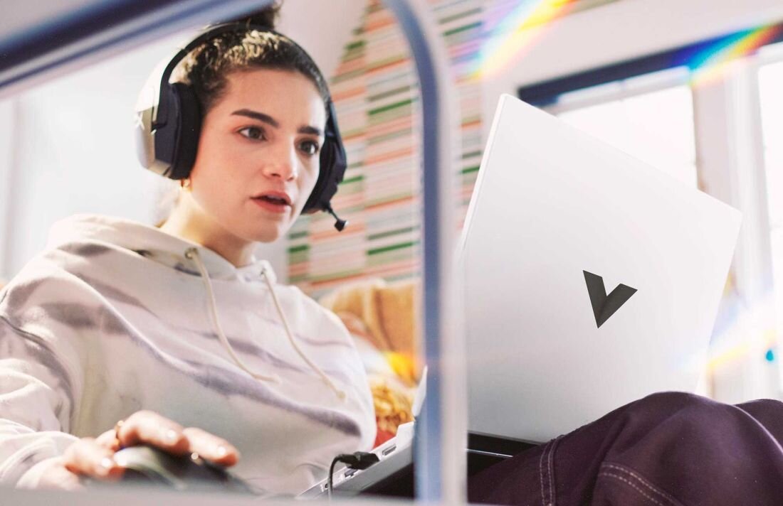 Laptop HP Victus 15 - Kobieta w białej bluzie i słuchawkach siedzi w autobusie z laptopem, skupiona na pracy lub relaksie. Ekologia w technologii
