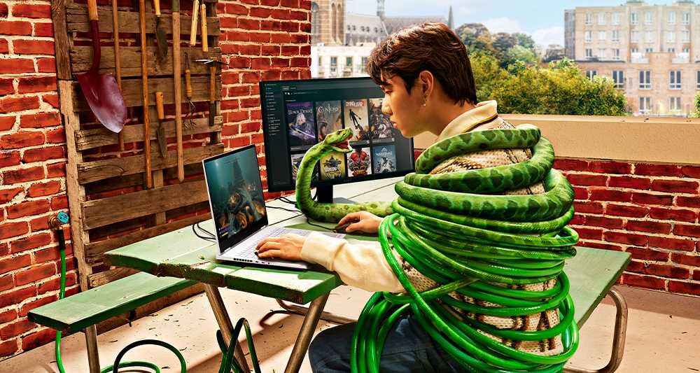 Mężczyzna przy stole z laptopem HP Omen 16, z zielonym wężem owiniętym wokół szyi. - Kamera HP TrueVision FHD