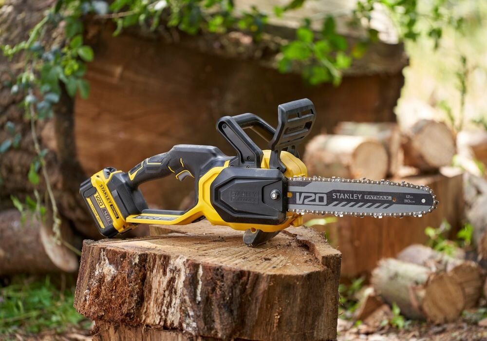 Piła akumulatorowa STANLEY 18V Fatmax V20 SFMCCS730B-XJ podwórko pnie drzew piła ustawiona na ścięty pniu drzewa w tle inne drewno liście wydajna praca w ogrodzie cięcie gałęzi cięcie drewna uniwersalność