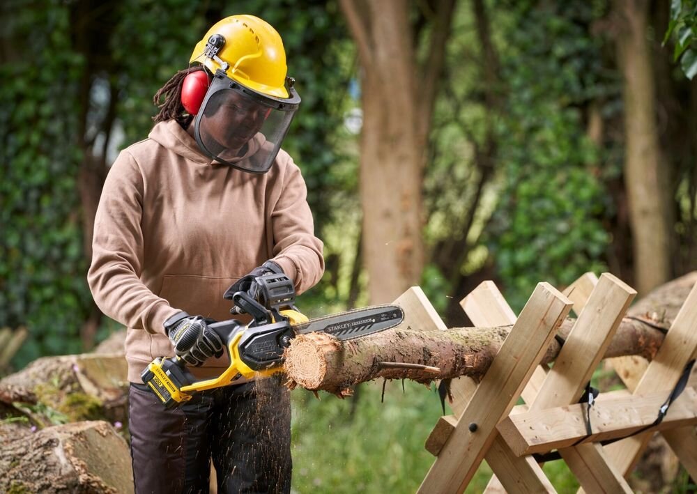 Piła akumulatorowa STANLEY 18V Fatmax V20 SFMCCS730B-XJ las osoba tnie pień drzewa w tle drzewa liście osoba w żółtym kasku zintegrowany system hamulca łańcucha szybkie zatrzymanie pracy w sytuacjach wymagających natychmiastowej reakcji duży uchwyt pomocniczy kontrola nad kierunkiem cięcia większa przewidywalność ruchów ograniczenie niepożądanych szarpnięć