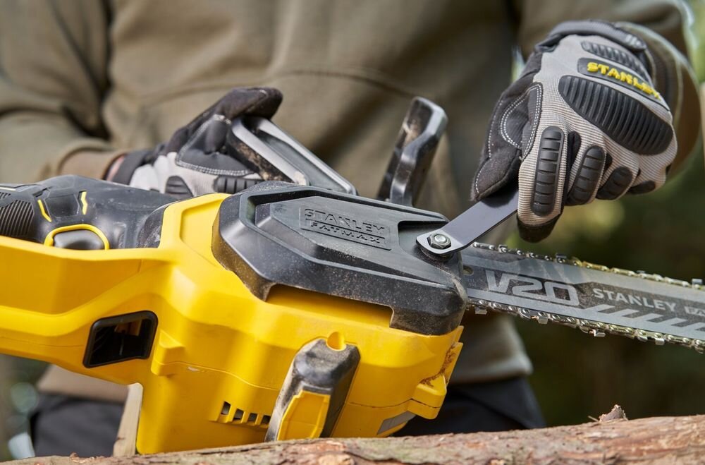 Piła akumulatorowa STANLEY 18V Fatmax V20 SFMCCS730B-XJ osoba trzyma piłę w dłoni reguluje za pomocą klucza łańcuch drewno drzewo funkcja napinanie łańcucha z blokadą śrubową precyzyjne dopasowanie naciągu do aktualnych warunków pracy równa linia cięcia ogranicza nadmierne zużycie łańcucha klucz przechowywany bezpośrednio na narzędziu