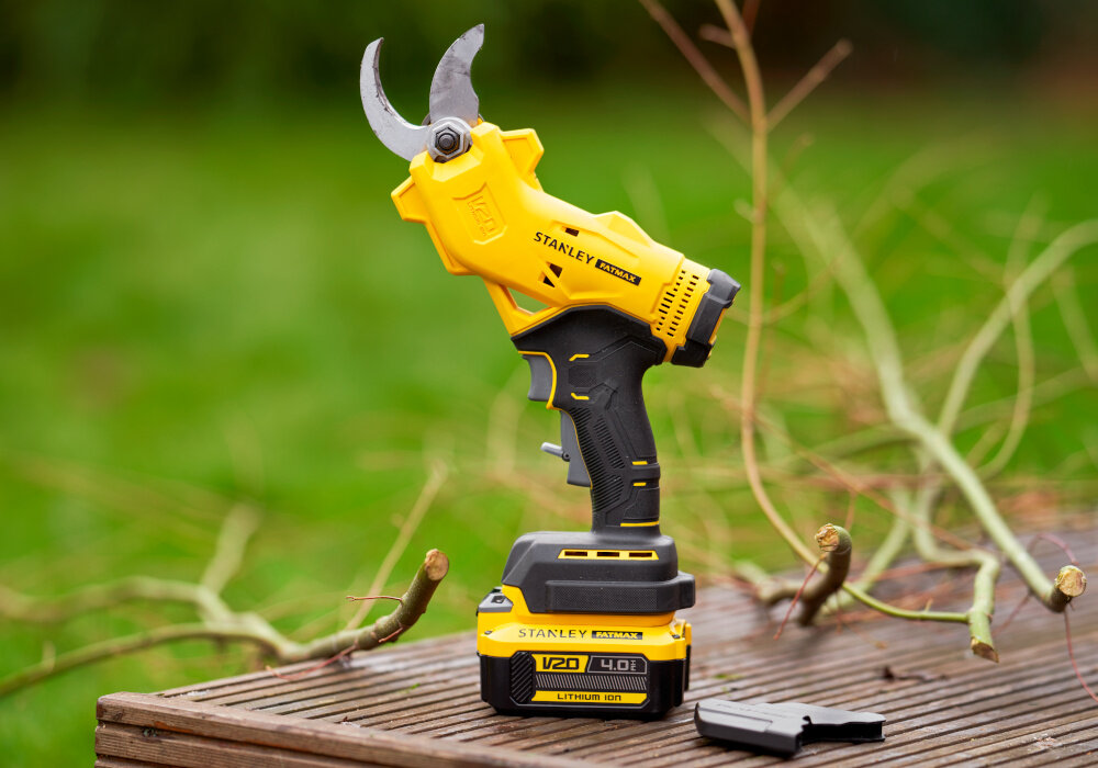 Sekator do gałęzi akumulatorowy STANLEY FatMax SFMCPP32M1-QW ogród drewniany podest na podeście stoi sekator obok leży osłona ostrza w tle trawnik sprawne cięcie gałęzi zadbany ogród przycinanie drzew krzewów kwiatów