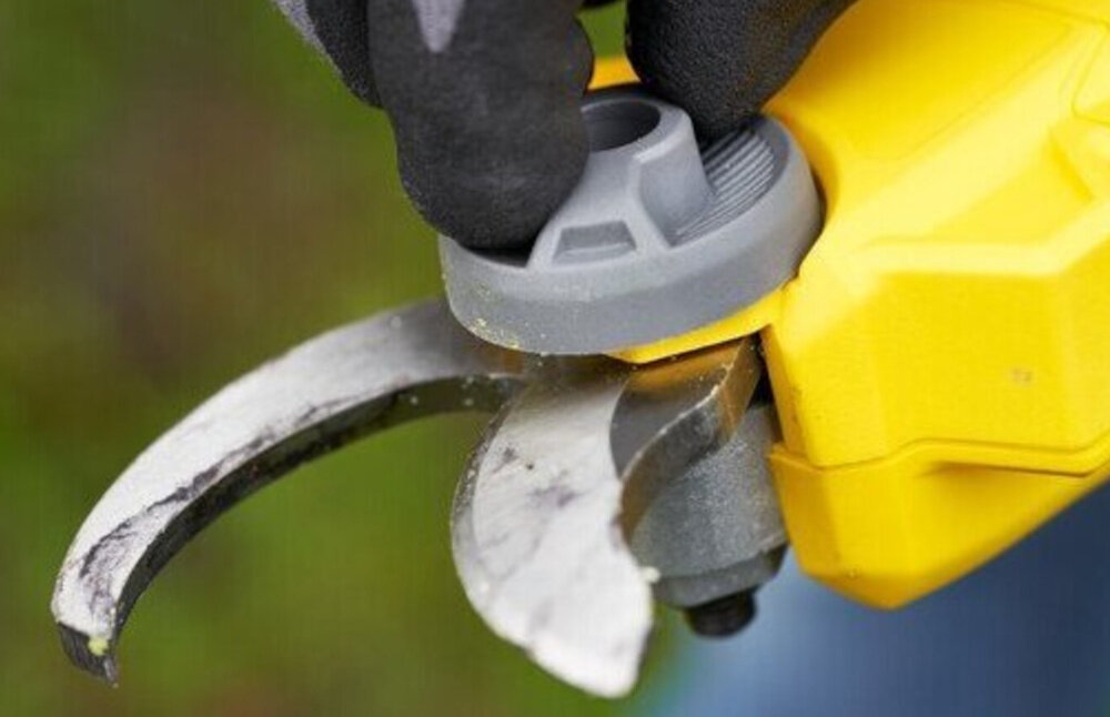 Sekator do gałęzi akumulatorowy STANLEY FatMax SFMCPP32M1-QW rozmazane tło osoba trzyma pokrętło do wymiany ostrza w dłoni beznarzędziowa wymiana ostrza ułatwia realizację prac pielęgnacyjnych bez długich przerw zwiększa wygodę użytkowania pozwala sprawniej reagować na zmienne warunki w ogrodzie