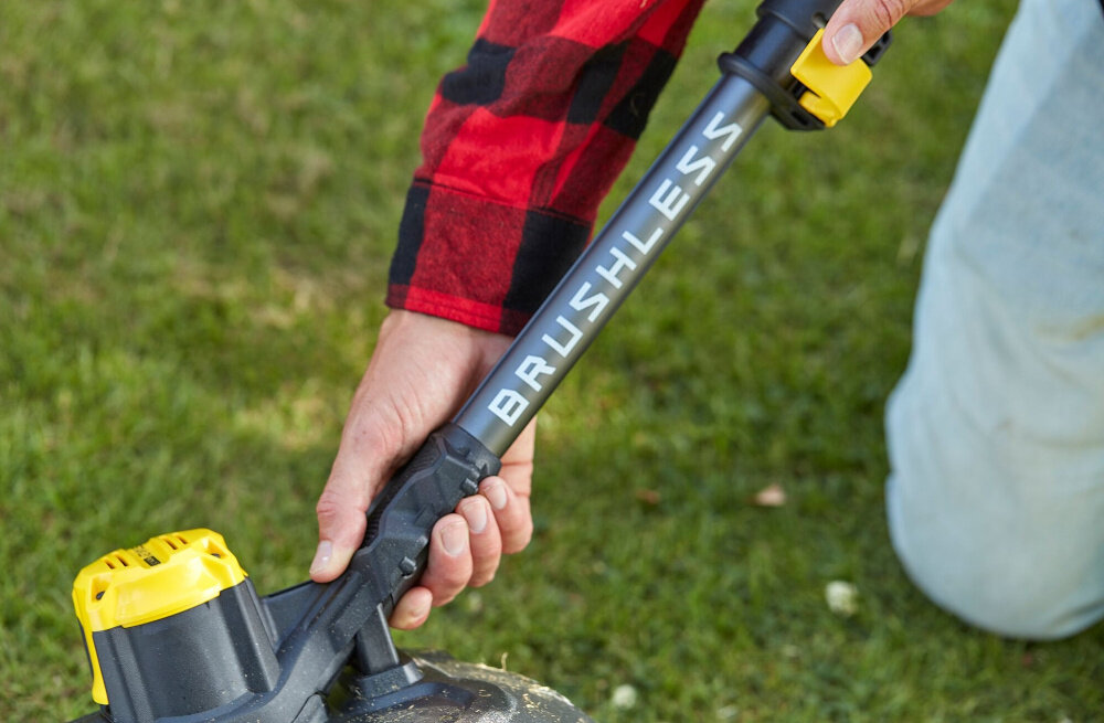 Podkaszarka akumulatorowa STANLEY SFMCSTB933B-XJ trawnik ogród osoba trzyma podkaszarkę w dłoni zbliżenie na trzonek na trzonku napis brushless silnik bezszczotkowy wyższa wydajność pracy mniejsze zużycie energii brak szczotek oznacza mniejszą potrzebę konserwacji dłuższa żywotność urządzenia stabilna moc