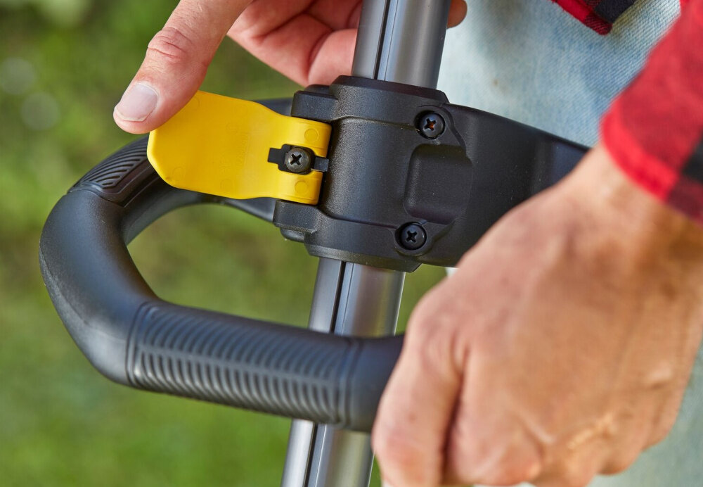 Podkaszarka akumulatorowa STANLEY SFMCSTB933B-XJ zbliżenie na uchwyt pomocniczy osoba reguluje uchwyt lekka konstrukcja o wadze 2,9 kg teleskopowy trzonek regulowany uchwyt pomocniczy zintegrowany wskaźnik naładowania akumulatora hak do zawieszania przechowywanie w systemie ściennym STANLEY Track