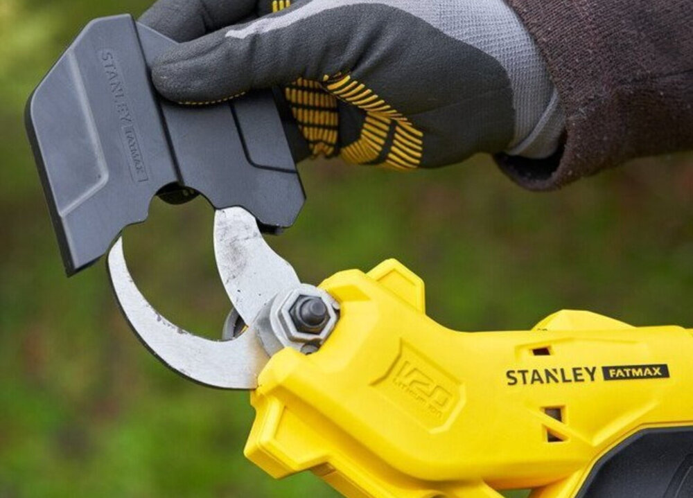 Sekator do gałęzi akumulatorowy STANLEY FatMax SFMCPP32B-XJ osoba trzyma sekator w dłoni zakłada osłonę na ostrze rozmazane tło osłona ostrza ochrona przed kurzem zabrudzeniami i wilgocią wydłuża żywotność ostrza utrzymuje je w pełnej sprawności zmniejsza ryzyko przypadkowego kontaktu z tnącym elementem bezpieczeństwo komfort