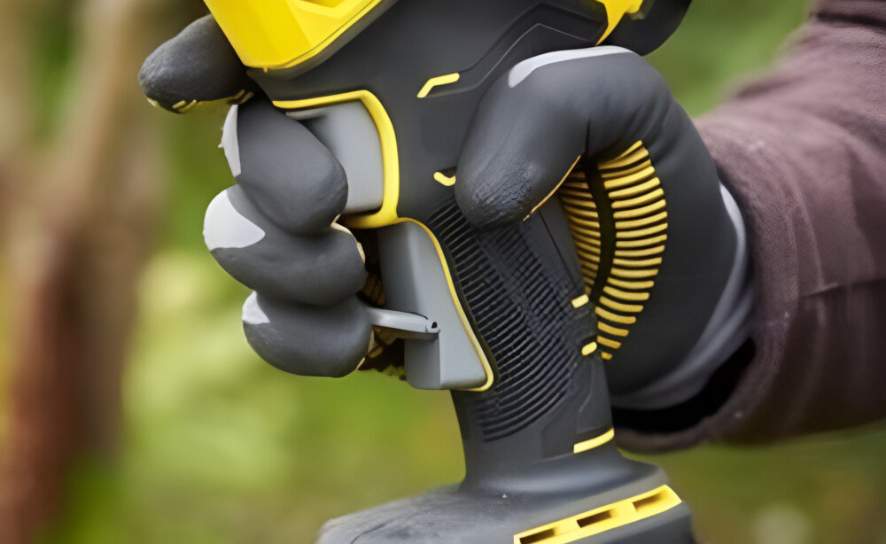 Sekator do gałęzi akumulatorowy STANLEY FatMax SFMCPP32B-XJ zbliżenie na rękojeść osoba trzyma dłoń na rękojeści w tle gałęzie ergonomiczna konstrukcja z gumowaną nakładką stabilność chwytu ogranicza ślizganie się dłoni podczas pracy dobrze wyważona forma waga 1,3 kg bez akumulatora ułatwia manewrowanie narzędziem