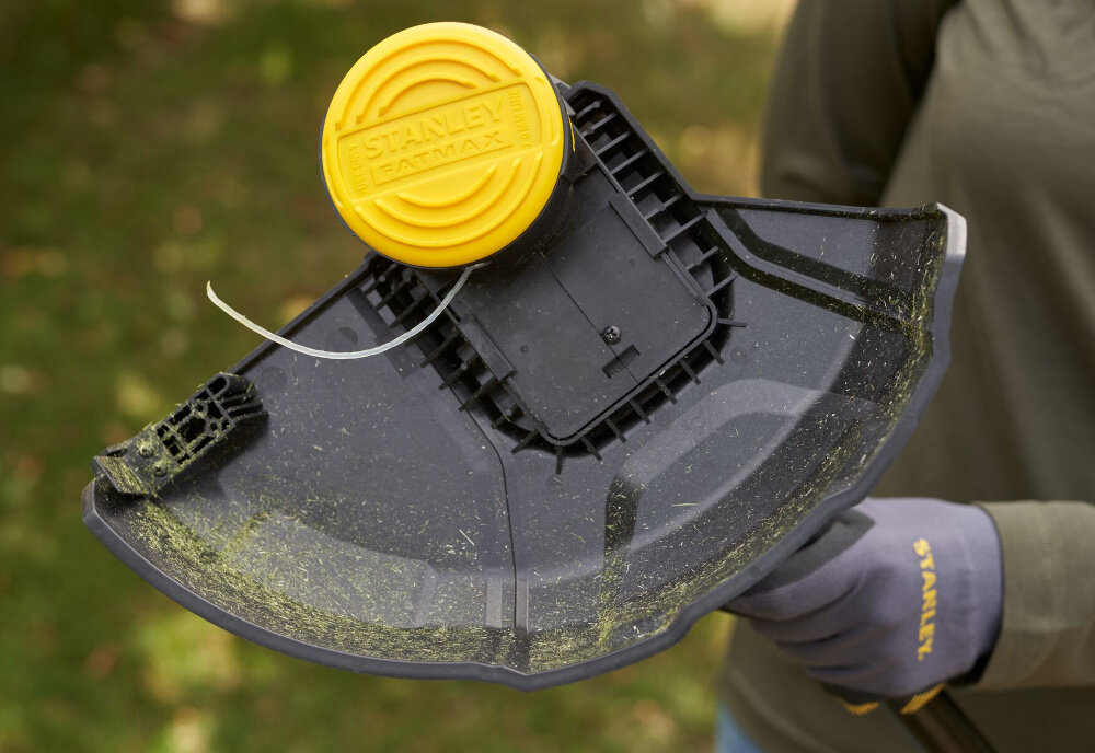 Podkaszarka akumulatorowa STANLEY SFMSTB930B-XJ rozmyte tło osoba trzyma podkaszarkę w dłoniach zbliżenie na moduł tnący jednoliniowy posuw żyłki o średnicy 2 mm automatyczne podawanie żyłki eliminuje konieczność ręcznych regulacji cięcie pozostaje równe