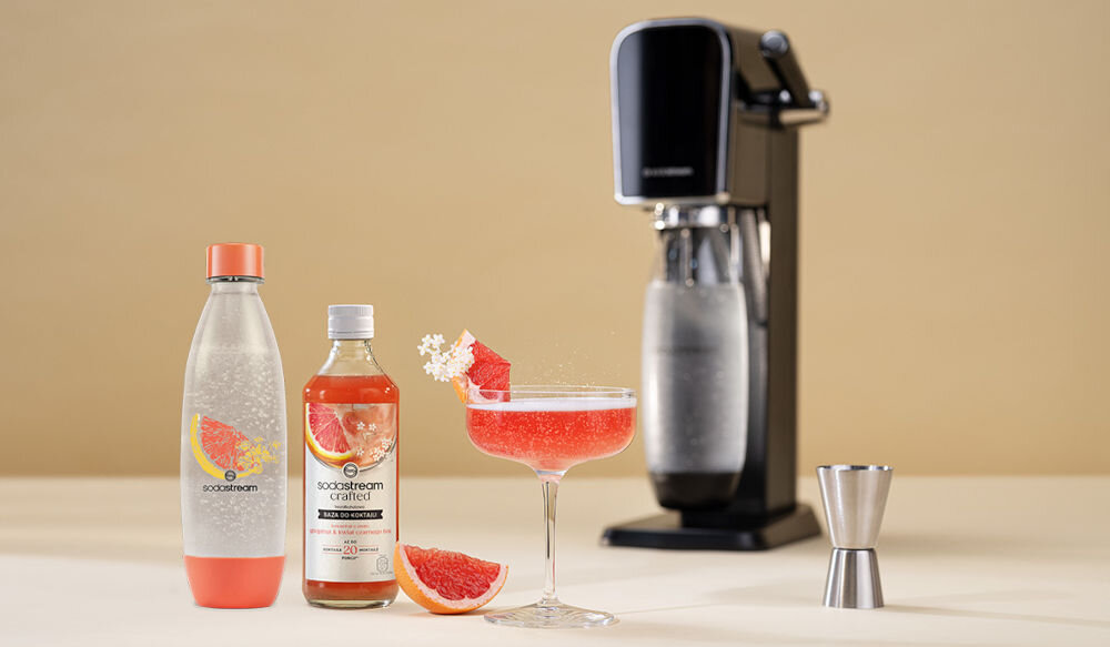 Zestaw upominkowy SODASTREAM Crafted Kit Coral jasne tło z tyłu stoi saturator butelka pomarańczowy spód pomarańczowa nakrętka czerwony napój w kieliszku kawałki grejpfruta kostki lodu troska o planetę krok w kierunku ekologii plastiku tritan do wielokrotnego użytkowania bezpieczeństwo wolna od BPA możliwość mycia w zmywarce świeżość na dłużej szczelny korek kompatybilność modele Terra, Art, Duo, Enso, Spirit i Source