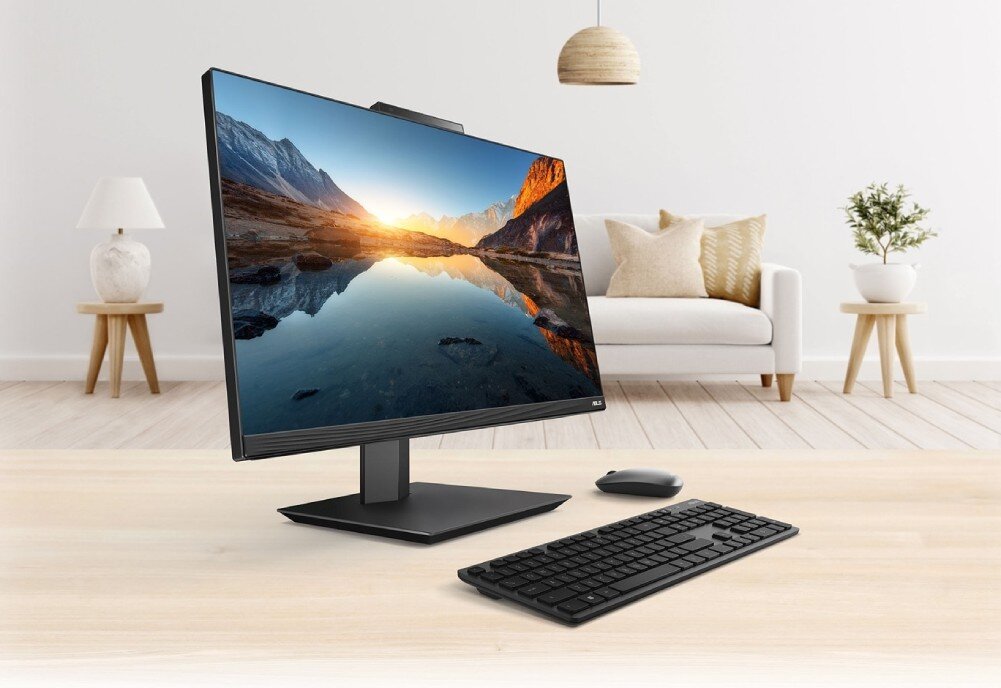 Komputer ASUS A5702WVARK-BPE014W Komputer All-in-One ustawiony na biurku wraz z klawiaturą i myszką na tle jasnego salonu, wyświetlający górski krajobraz