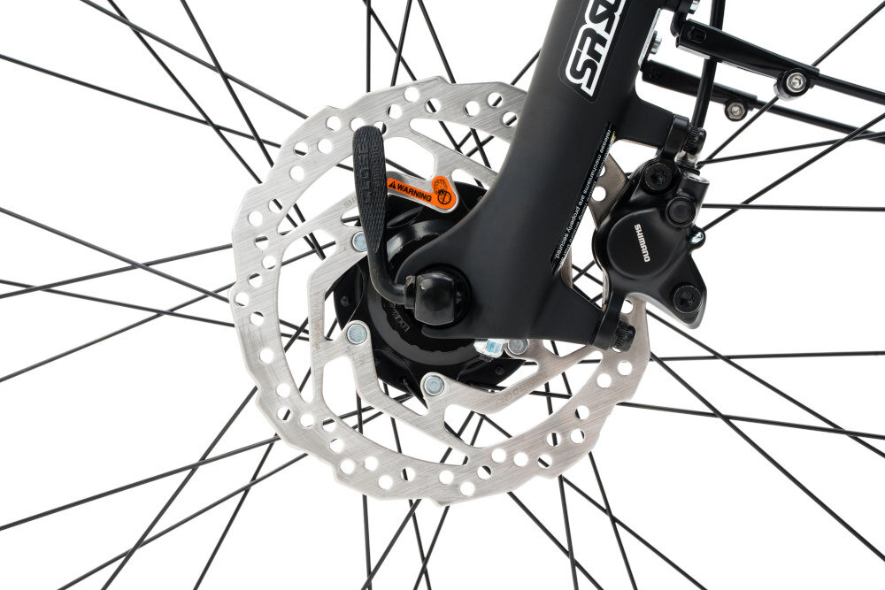 Zbliżenie na tarczę hamulcową roweru z widocznym zaciskiem hamulcowym marki Shimano. Na widelcu znajduje się napis \'SR SUNTOUR\'.