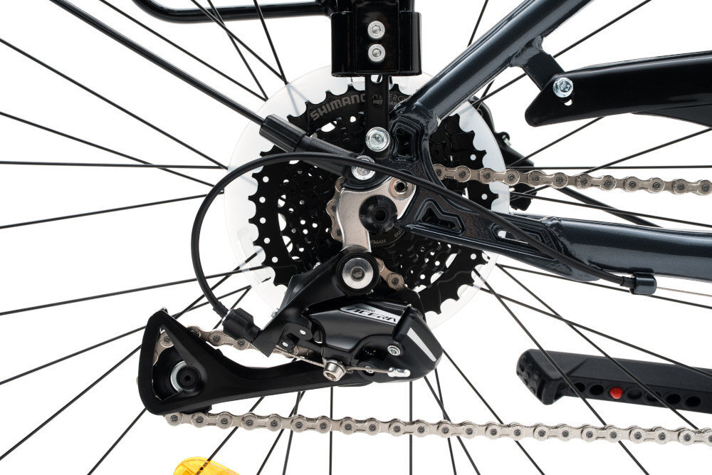 Zdjęcie przedstawia mechanizm przerzutki rowerowej z widocznym napisem \'SHIMANO\'. W tle widać zębatki i łańcuch rowerowy.
